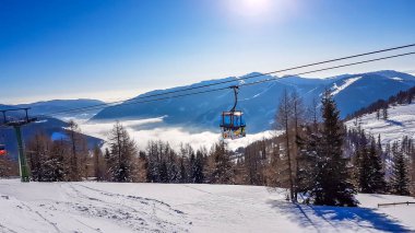 A cable car going up in Bad Kleinkirchheim, Austria. Big ski resort. The slopes are perfectly gravelled. Some trees on the side. There is a fog in the valley. Winter sports. Clear and bright day.