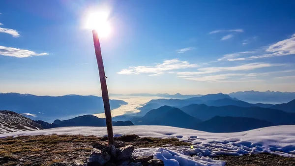 A pole on top of a fog covered, snowy Alps in Goldeck, Austria. The sun shines exactly on top of the pole. Crispy and frosty morning. endless mountain chains in the back. Ground is covered with snow.