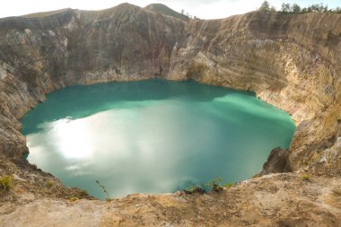 Close up view on the Kelimutu volcanic crater lakes in Flores Indonesia. Lakes are shining with many shades of turquoise and blue. Sun shines through clouds. Barren and sharp slopes of volcanic crater