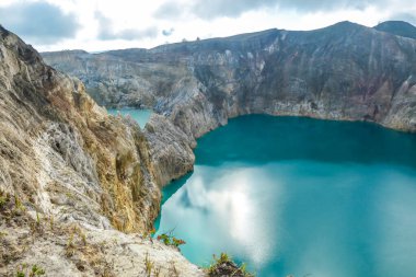 Close up view on the Kelimutu volcanic crater lakes in Flores Indonesia. Lakes are shining with many shades of turquoise and blue. Sun shines through clouds. Barren and sharp slopes of volcanic crater