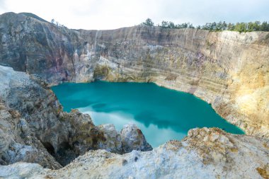 Close up view on the Kelimutu volcanic crater lakes in Flores Indonesia. Lakes are shining with many shades of turquoise and blue. Sun shines through clouds. Barren and sharp slopes of volcanic crater