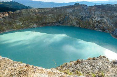 Close up view on the Kelimutu volcanic crater lakes in Flores Indonesia. Lakes are shining with many shades of turquoise and blue. Sun shines through clouds. Barren and sharp slopes of volcanic crater