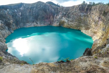 Close up view on the Kelimutu volcanic crater lakes in Flores Indonesia. Lakes are shining with many shades of turquoise and blue. Sun shines through clouds. Barren and sharp slopes of volcanic crater