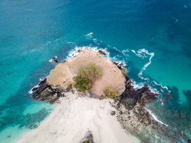 A top-down drone shot of an idyllic Koka Beach. Hidden gem of Flores, Indonesia. Headland going straight into the open sea. Beauty in the nature. Calm waves washing the cliff's slopes. Serenity.