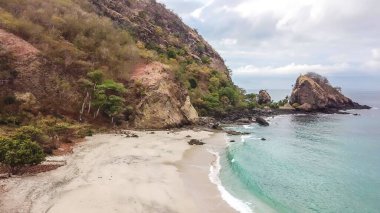 A view on an idyllic Koka Beach. Hidden gem of Flores, Indonesia. Steep slopes of the hills joining the sea. Waves gently washing the shore. There are hills in the back. Happiness and love