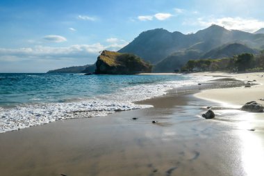 A black and white sand beach, gently washed by waves on an idyllic Koka Beach. Hidden gem of Flores, Indonesia. There are some boulders in the sea. Escaping from it all. Beauty in the nature