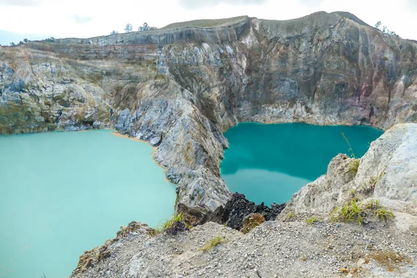 Close up view on the Kelimutu volcanic crater lakes in Flores Indonesia. Lakes are shining with many shades of turquoise and blue. Sun shines through clouds. Barren and sharp slopes of volcanic crater