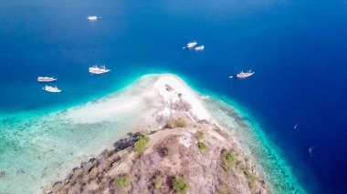 Top down drone shot of a paradise island with some boats anchored around in Komodo National Park, Flores, Indonesia. Brownish island turns into white sand beach and further into turquoise and navy sea