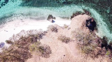 Top down drone shot of a paradise island with some boats anchored around in Komodo National Park, Flores, Indonesia. Brownish island turns into white sand beach and further into green and navy sea