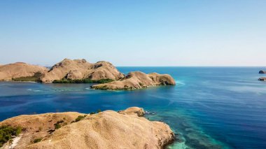 A drone shot of two bigger paradise islands in Komodo National Park, Flores, Indonesia. The islands have scarcely any trees and bushes. Dry land. Idyllic white sand beaches. Island hoping