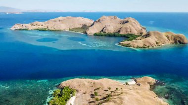 A drone shot of two bigger paradise islands in Komodo National Park, Flores, Indonesia. The islands have scarcely any trees and bushes. Dry land. Idyllic white sand beaches. Island hoping