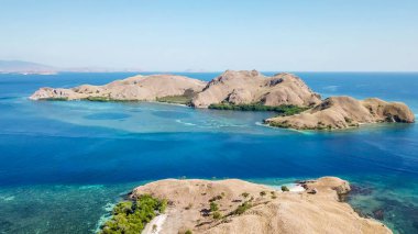 A drone shot of two bigger paradise islands in Komodo National Park, Flores, Indonesia. The islands have scarcely any trees and bushes. Dry land. Idyllic white sand beaches. Island hoping