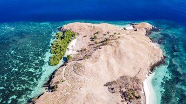 A top down drone shot of paradise island in Komodo National Park, Flores, Indonesia. The island has scarcely any trees and bushes and is surrounded with idyllic white sand beaches. Island hoping