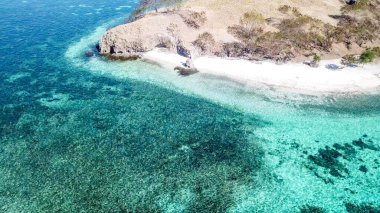 A drone shot of a paradise island in Komodo National Park, Flores, Indonesia. Brownish island turns into white sand beach and further into turquoise and navy blue sea. Steep slopes of the island