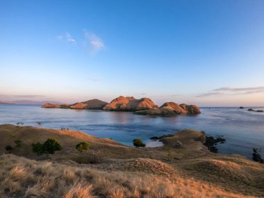 A view on a the morning sun rising over an island formation in Komodo National Park, Flores, Indonesia. Golden hour over the islands and sea. Idyllic landscape. New day beginning. Chocolate hills.