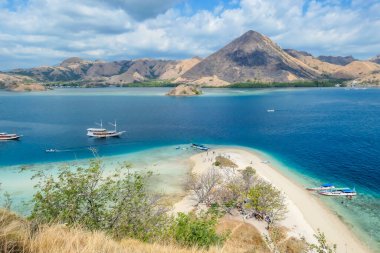 View from top of a cliff on Kelor Island, Komodo, Indonesia. Island is surrounded with white sand beaches and turquoise water. There is another island in the back.There are boats anchored to a shore.