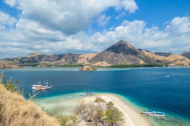 View from top of a cliff on Kelor Island, Komodo, Indonesia. Island is surrounded with white sand beaches and turquoise water. There is another island in the back.There are boats anchored to a shore.