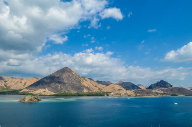 View from top of a cliff on Kelor Island, Komodo, Indonesia. Island is surrounded with white sand beaches and turquoise water. There is another island in the back.There are boats anchored to a shore.