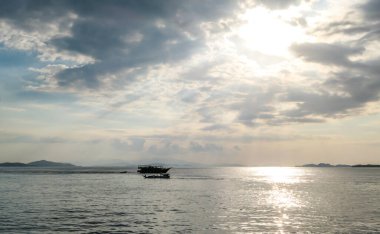 Sunbeams breaking out through the clouds and reaching the calm surface of the sea in Komodo National Park, Indonesia. There are some islands in the back. Small boat crossing the sea. Island hoping