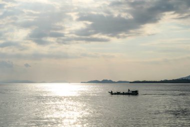 Sunbeams breaking out through the clouds and reaching the calm surface of the sea in Komodo National Park, Indonesia. There are some islands in the back. Small boat crossing the sea. Island hoping