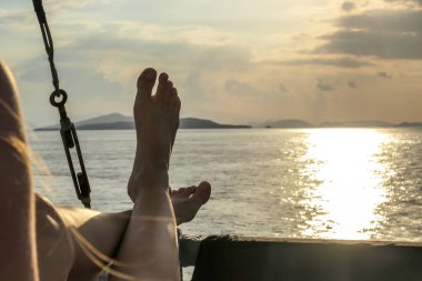 A pair of woman's leg hanging over the rail of small boat, enjoying beautiful sunset in Komodo National Park, Flores, Indonesia. Sun sets over the horizon line. Having a relaxed time.