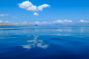 Calm surface of the sea reflecting the sky in Komodo National Park, Indonesia. The sea surface is almost exact copy of the sky. There is an island in the back. Heart shaped cloud.