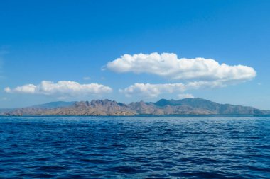 A view on idyllic island in Komodo National Park, Indonesia. There are few clouds above the island. Calm and clear surface of the sea. Island hoping. Perfect day for sailing