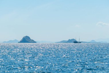 Sunbeams breaking out through the clouds and reaching the calm surface of the sea in Komodo National Park, Indonesia. There are some islands in the back. Small boat crossing the sea. Island hoping