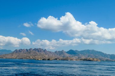 A view on idyllic island in Komodo National Park, Indonesia. There are few clouds above the island. Calm and clear surface of the sea. Island hoping. Perfect day for sailing