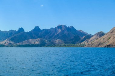 A view on idyllic island in Komodo National Park, Indonesia. There are few clouds above the island. Calm and clear surface of the sea. Island hoping. Perfect day for sailing