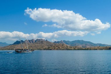 A view on idyllic island in Komodo National Park, Indonesia. There are few clouds above the island. Calm and clear surface of the sea. Island hoping. Perfect day for sailing