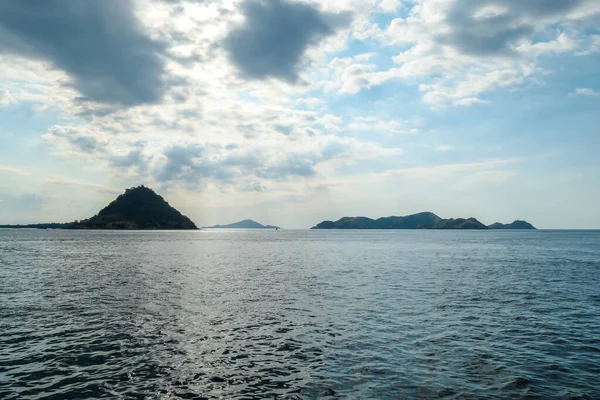 Sunbeams breaking out through the clouds and reaching the calm surface of the sea in Komodo National Park, Indonesia. There are some islands in the back. Island hoping
