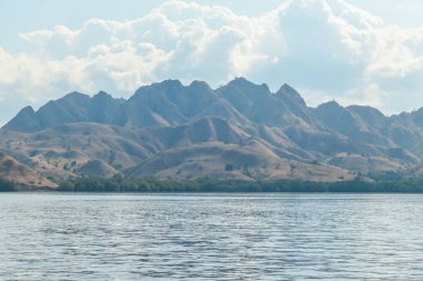 A view on idyllic island in Komodo National Park, Indonesia. There are few clouds above the island. Calm and clear surface of the sea. Island hoping. Perfect day for sailing