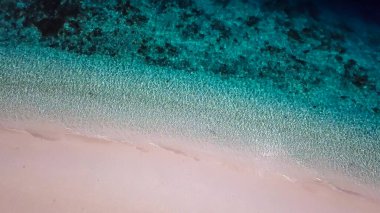 A drone shot of a pink sand beach on a small island near Maumere, Indonesia. Happy and careless moments. Waves gently washing the shore.Clear, turquoise coloured water displaying coral reef.