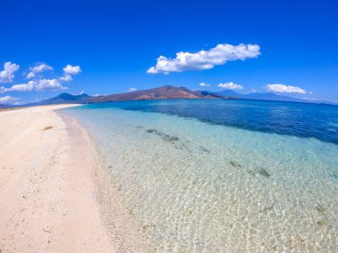 A view on white sand beach on a small island near Maumere, Indonesia. Happy and careless moments. Waves gently washing the shore. Clear, turquoise coloured water displaying coral reef. Hidden gem.