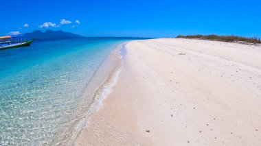 A view on white sand beach on a small island near Maumere, Indonesia. Happy and careless moments. Waves gently washing the shore. Clear, turquoise coloured water displaying coral reef. Hidden gem.