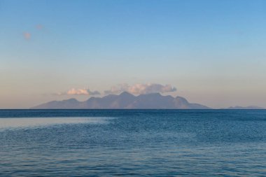 A soft coloured sky during the sunset in Maumere, Flores, Indonesia. Calm surface of the sea. There is a big island over the horizon. Cotton candy sky. Serenity and calmness.