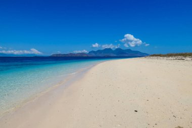 A view on white sand beach on a small island near Maumere, Indonesia. Happy and careless moments. Waves gently washing the shore. Clear, turquoise coloured water displaying coral reef. Hidden gem.