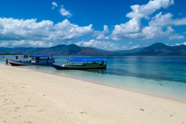 Two boats anchored to white sand beach on an island near Maumere, Indonesia. There is a fishing cottage on the side. Clear, turquoise coloured water displaying coral reef
