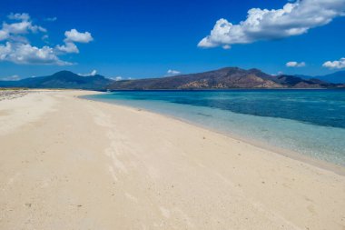 A view on white sand beach on a small island near Maumere, Indonesia. Happy and careless moments. Waves gently washing the shore. Clear, turquoise coloured water displaying coral reef. Hidden gem.