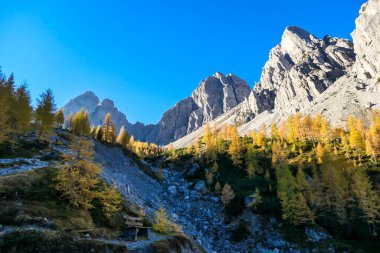 A panoramic view on Lienz Dolomites, Austria, bathing in the morning sun. The sun beams are coming into the valley through high mountain peaks. The valley is green, contrasting with barren rocks.