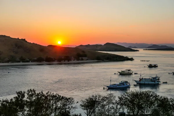 A view on a the morning sun rising over an island formation in Komodo National Park, Flores, Indonesia. Golden hour over the islands and sea. There are few boats anchored to the shores of the islands.