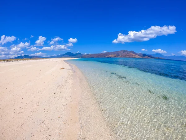 A view on white sand beach on a small island near Maumere, Indonesia. Happy and careless moments. Waves gently washing the shore. Clear, turquoise coloured water displaying coral reef. Hidden gem.