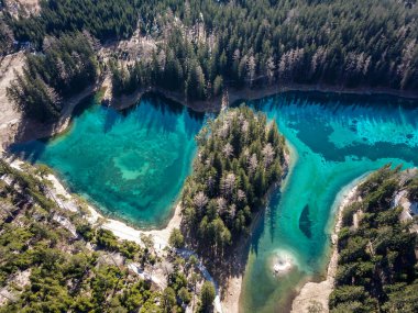 A drone shot of anAlpine valley in Austria. The valley has a Green Lake in the middle.  A headland in the middle of the lake. The algae give the lake distinctive color. Early spring in the mountains