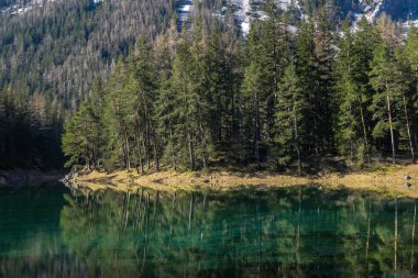 A view on an Alpine valley in Austria. The valley has a Green Lake in the middle. Early spring in the mountains. There is a high mountain range in the back. Freshness. Dense forest around the lake