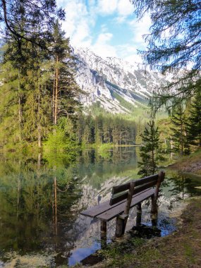A bench partially flooded by water in the middle of Green Lake, Austria. Early spring in the mountains. The lake collects the water from melting glaciers. Dense forest around the lake