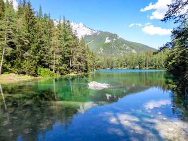 A peaceful view on an Alpine valley in Austria. The valley has a Green Lake in the middle. Early spring in the mountains. There is a high mountain range in the back. Freshness. Few ducks on the lake.