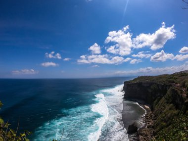 A done shot of Uluwatu Cliffs, Bali, Indonesia. The waves are rushing to the shore, making the water bubbly. The beach is covered with green algae, further on it's sandy. Hidden gem of Indonesia.