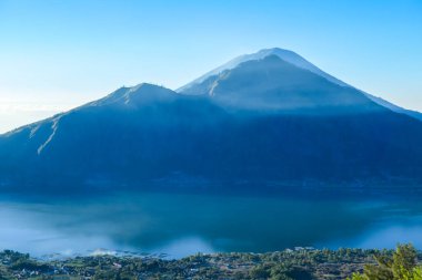 An idyllic view from the top of Mount Batur on Mount Agung and the Danau Batur lake. There is a pathway along Batur volcano's rim. Volcanic landscape of Bali, Indonesia. Island hiking.