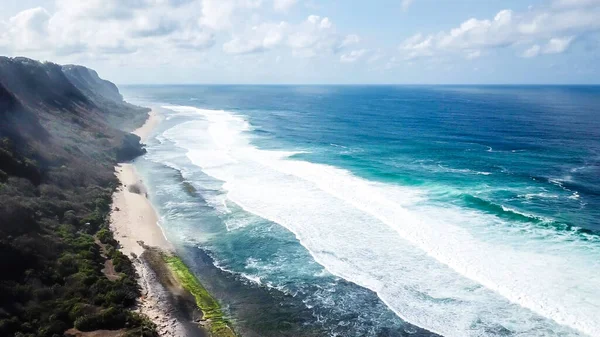 stock image A done shot of Nyang Nyang Beach, Bali, Indonesia. The waves are rushing to the shore, making the water bubbly. The beach is covered with green algae, further on it's sandy. Tall cliffs on the side